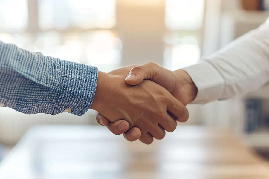 Young American man shaking hands across a light wood desk, a first loan agreed